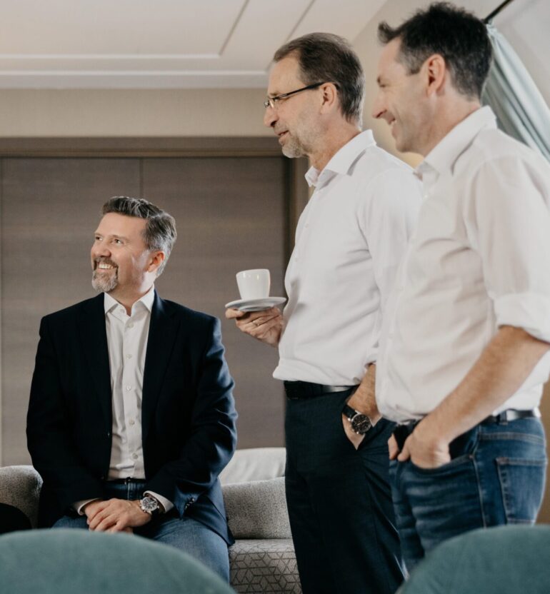 3 Personen unterhalten sich stehend und sitzend auf einem Sofa
